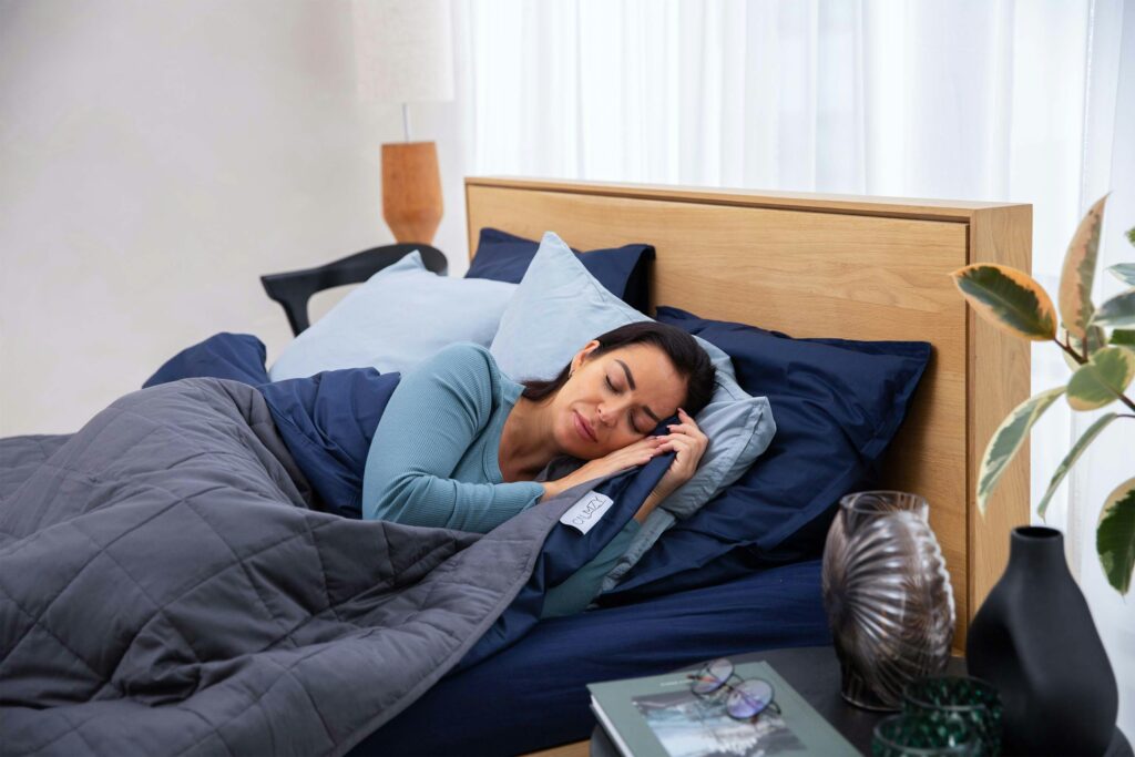 Une femme dort de coté dans un lit bleu marin avec les mains sous sa tête